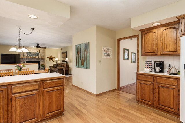 kitchen featuring brown cabinets, light wood finished floors, a fireplace, light countertops, and open floor plan