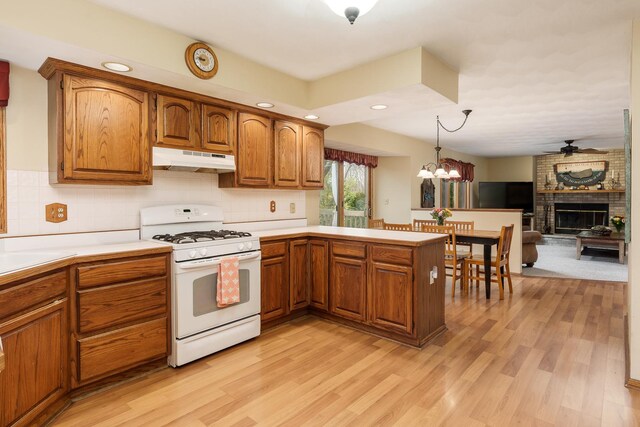 kitchen featuring light countertops, white gas range oven, ceiling fan with notable chandelier, light wood finished floors, and under cabinet range hood