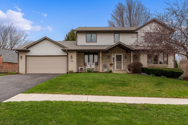 traditional-style home with covered porch, aphalt driveway, brick siding, a front lawn, and an attached garage