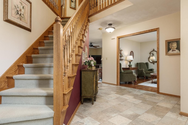 stairway featuring baseboards, a ceiling fan, and stone finish floor