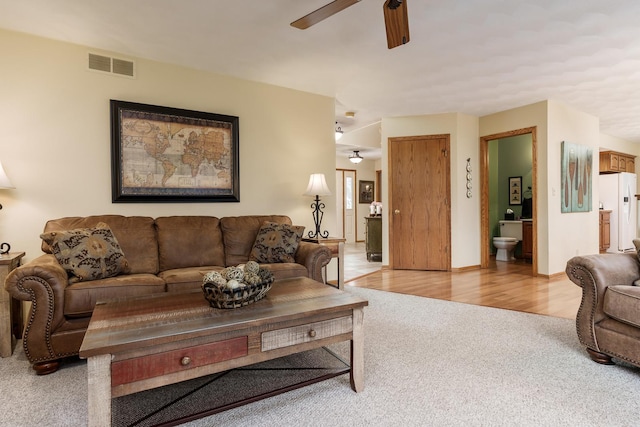 living room with ceiling fan, visible vents, and light carpet