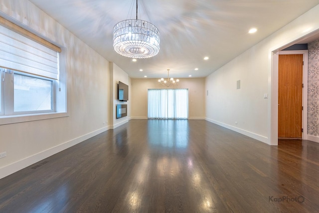 unfurnished living room with an inviting chandelier, plenty of natural light, wood finished floors, and visible vents