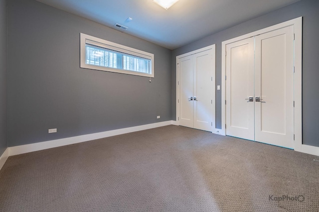 unfurnished bedroom featuring carpet floors, baseboards, multiple closets, and visible vents