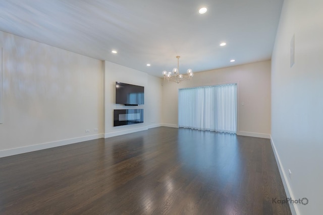 unfurnished living room with baseboards, dark wood-type flooring, recessed lighting, and a notable chandelier