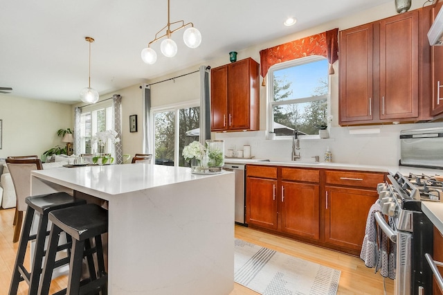 kitchen featuring light wood-style floors, a kitchen breakfast bar, stainless steel range with gas stovetop, a sink, and hanging light fixtures