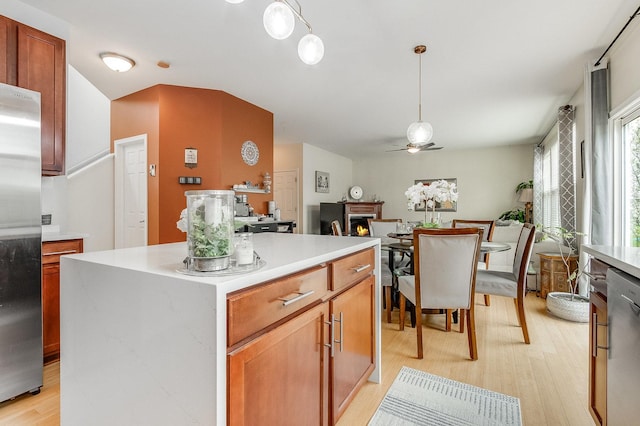 kitchen featuring ceiling fan, appliances with stainless steel finishes, light countertops, a warm lit fireplace, and light wood-style floors