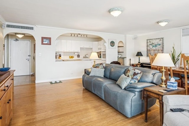 living room with crown molding, arched walkways, baseboards, light wood-type flooring, and visible vents
