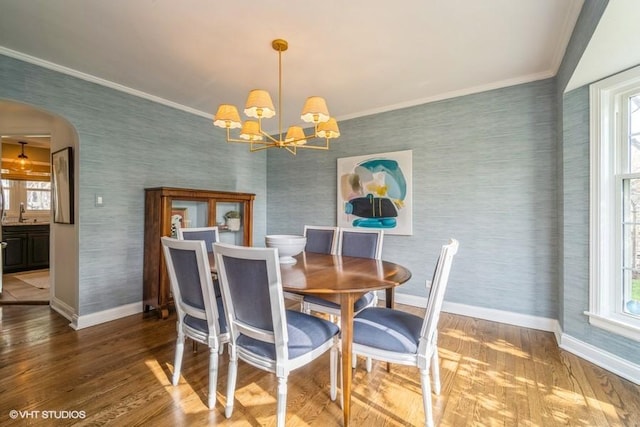 dining room featuring baseboards, wood finished floors, wallpapered walls, and arched walkways