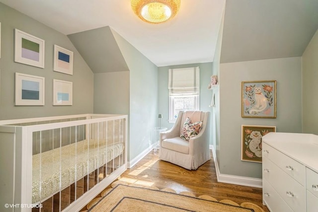 bedroom featuring vaulted ceiling, baseboards, a crib, and wood finished floors