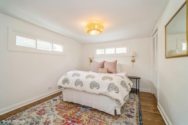 bedroom with multiple windows, a closet, wood finished floors, and baseboards