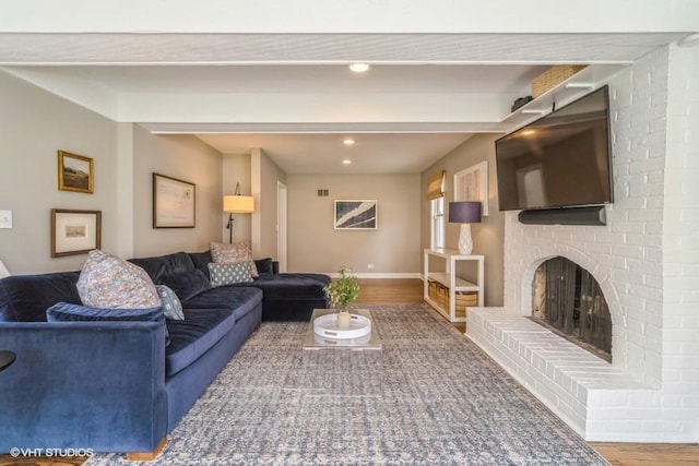 living area featuring beamed ceiling, wood finished floors, baseboards, and a fireplace