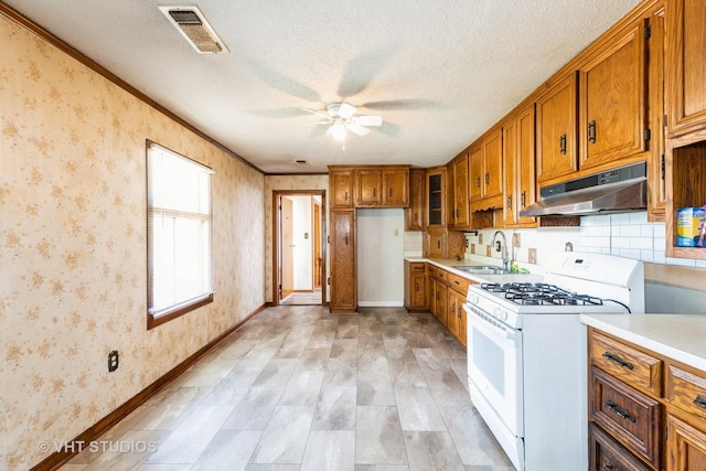 21822 Merrill Ave, Sauk Village, IL 60411 - kitchen with under cabinet range hood, white range with gas cooktop, a sink, brown cabinetry, and a ceiling fan