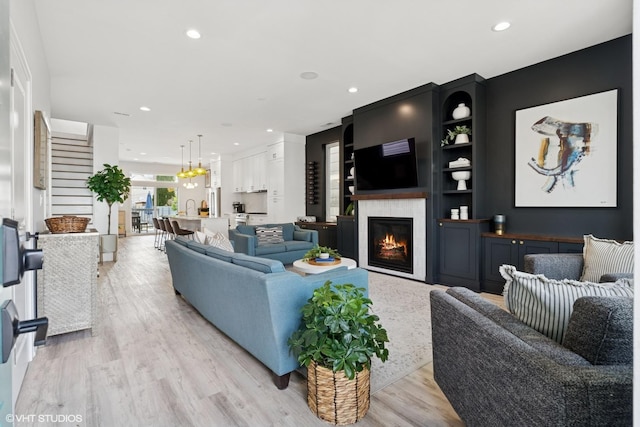 living area featuring recessed lighting, a glass covered fireplace, and light wood-type flooring