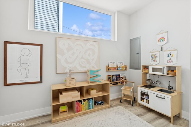rec room featuring a sink, baseboards, electric panel, and light wood finished floors