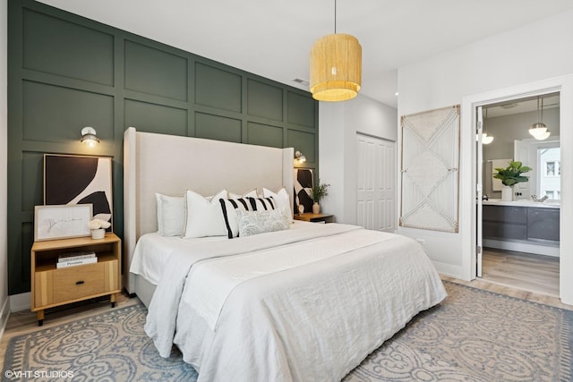 bedroom with a closet, a decorative wall, ensuite bathroom, a sink, and light wood finished floors