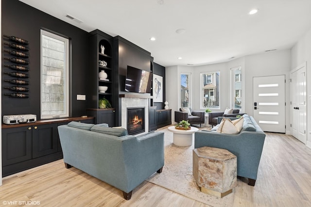 living room featuring visible vents, recessed lighting, light wood-style flooring, and a glass covered fireplace