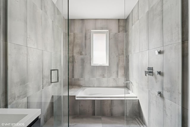 bathroom featuring tile walls, tiled bath, vanity, and tiled shower