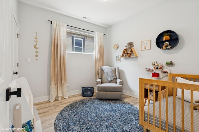 bedroom with a nursery area, baseboards, wood finished floors, and visible vents