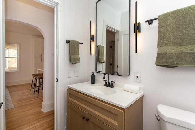 half bath featuring vanity, baseboards, toilet, and wood finished floors