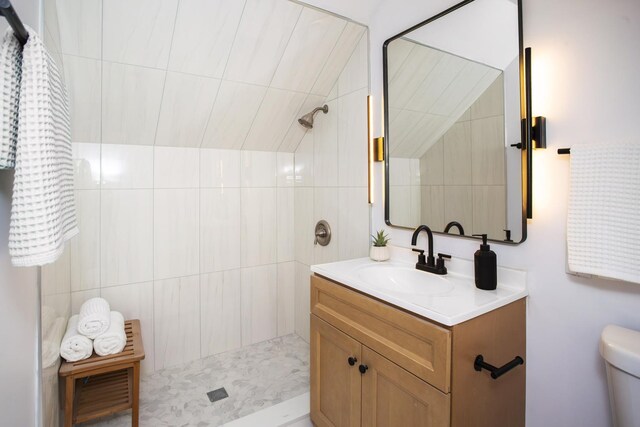 full bathroom featuring vanity, a tile shower, and toilet