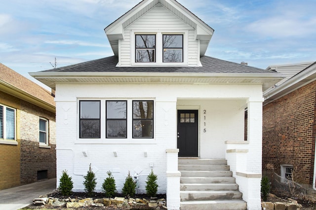 bungalow with a porch, brick siding, and a shingled roof