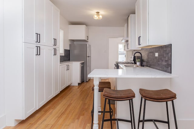 kitchen with a peninsula, a breakfast bar area, a sink, appliances with stainless steel finishes, and backsplash