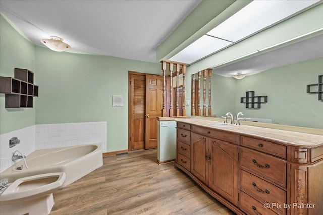 bathroom with a bidet, wood finished floors, a bath, and vanity