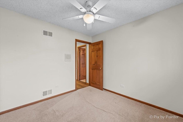carpeted spare room with visible vents, baseboards, and ceiling fan