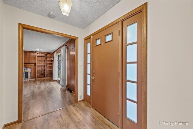 entrance foyer with visible vents, a brick fireplace, wood finished floors, baseboards, and a textured ceiling