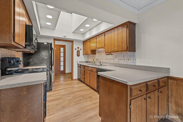kitchen featuring a sink, light wood finished floors, brown cabinetry, a tray ceiling, and black appliances