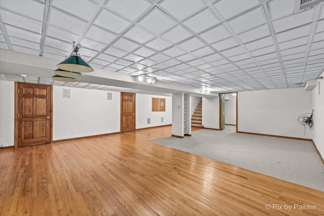 finished below grade area featuring baseboards, light wood-type flooring, stairs, and visible vents
