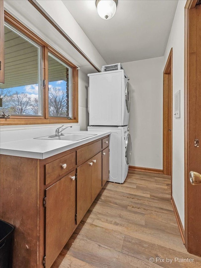 clothes washing area with stacked washer / dryer, cabinet space, a sink, baseboards, and light wood finished floors