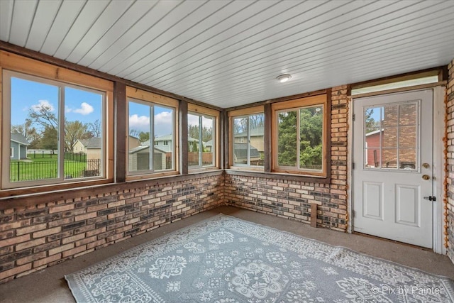 unfurnished sunroom featuring carpet floors, brick wall, and wooden ceiling