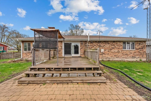rear view of property featuring a lawn, brick siding, a sunroom, and a deck