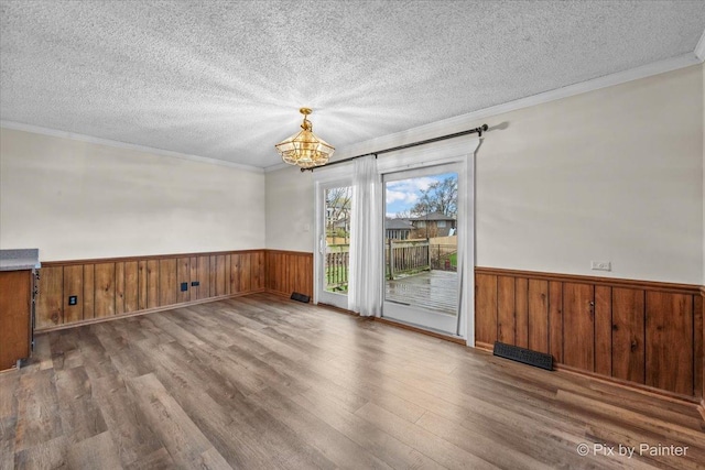 spare room with wood finished floors, ornamental molding, a wainscoted wall, and a notable chandelier