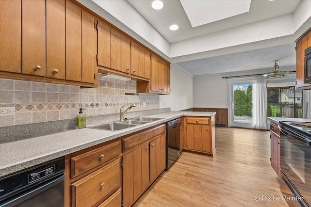 kitchen with brown cabinets, a sink, light wood-style floors, a wainscoted wall, and black appliances