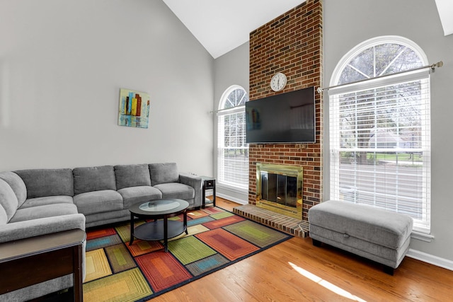 living area featuring baseboards, a brick fireplace, wood finished floors, and high vaulted ceiling