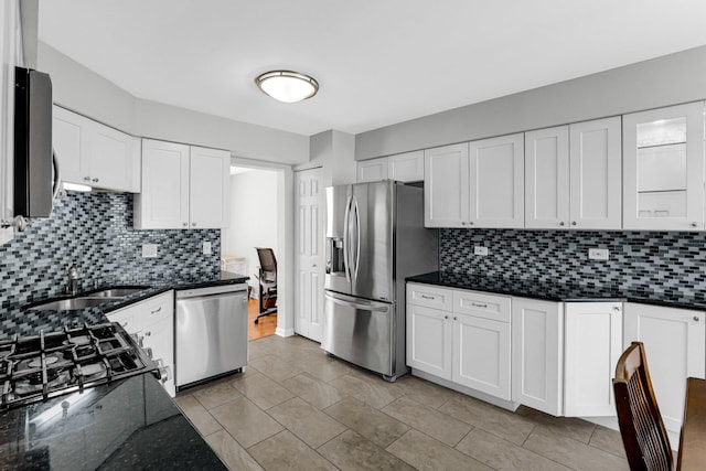 kitchen with dark stone counters, white cabinets, a sink, appliances with stainless steel finishes, and backsplash