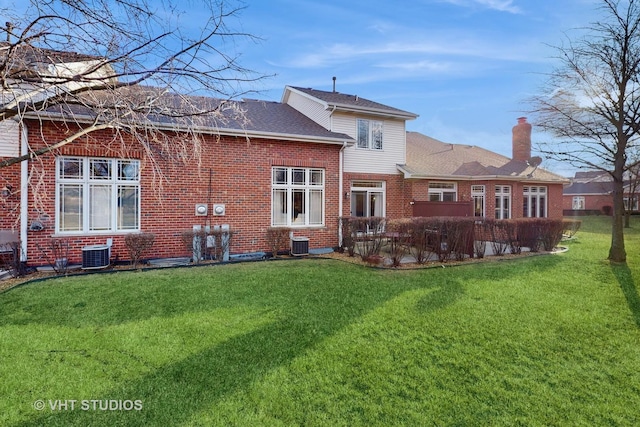back of property with central AC unit, a chimney, a yard, and brick siding