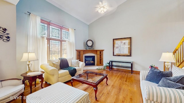 living area featuring crown molding, a glass covered fireplace, stairs, lofted ceiling, and light wood-type flooring