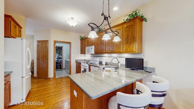 kitchen featuring brown cabinets, a sink, a peninsula, light wood-style floors, and white appliances