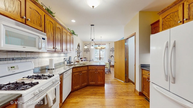 kitchen featuring a sink, light wood finished floors, brown cabinetry, and white appliances