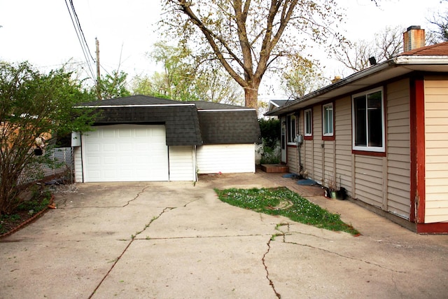 view of side of home with a garage, a shingled roof, and an outbuilding