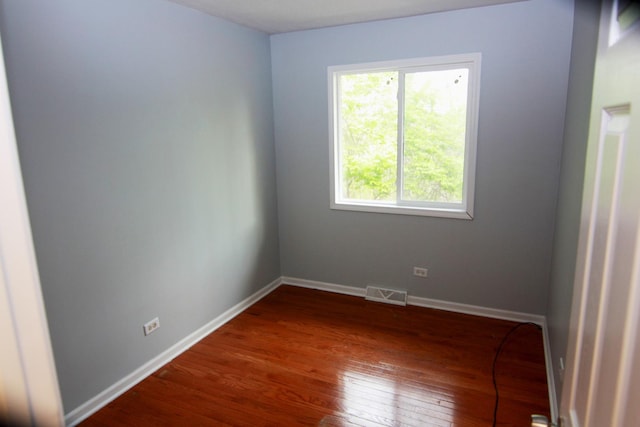 empty room featuring visible vents, baseboards, dark wood-type flooring, and a healthy amount of sunlight