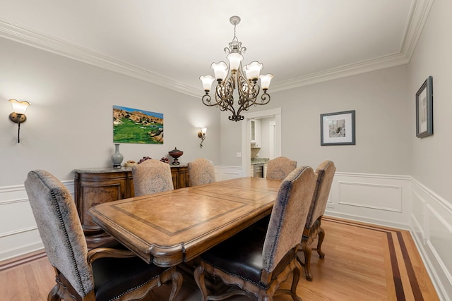 dining area with a chandelier, crown molding, light wood-type flooring, wainscoting, and a decorative wall