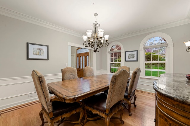 dining room with a chandelier, crown molding, light wood-type flooring, and a wainscoted wall