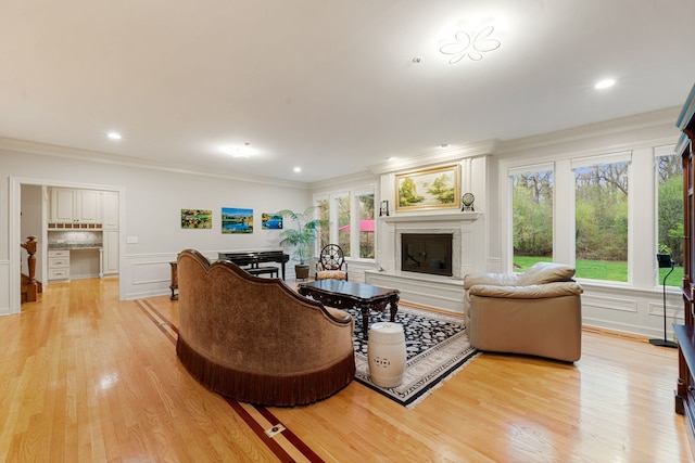 living room with ornamental molding, a glass covered fireplace, healthy amount of natural light, light wood-style floors, and a decorative wall