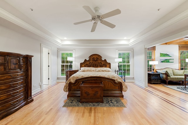 bedroom with a tray ceiling, light wood finished floors, multiple windows, and crown molding