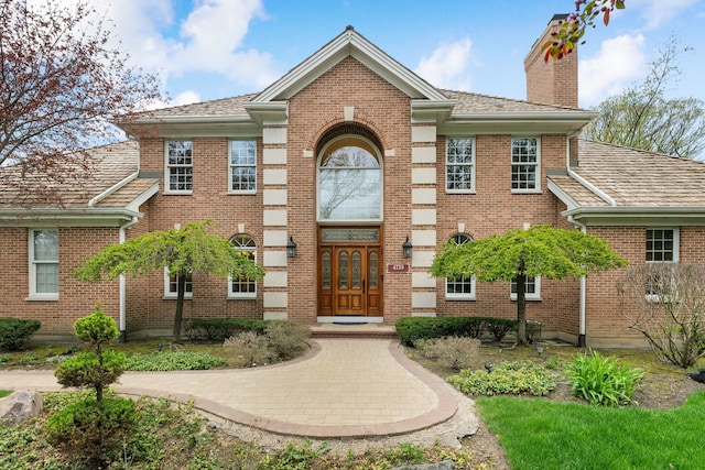 view of front of property featuring a chimney, brick siding, and french doors