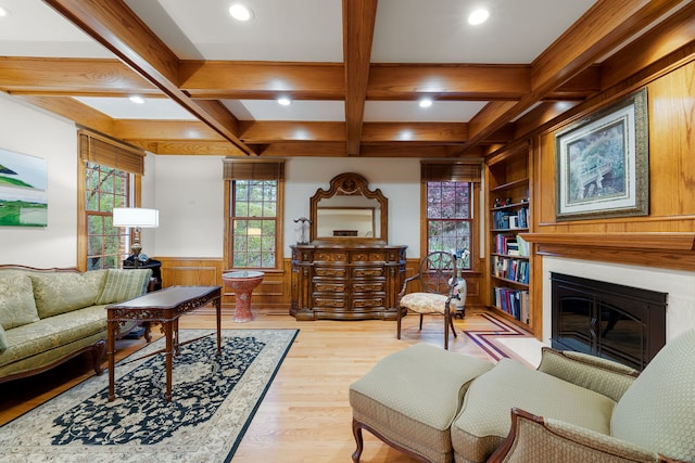 living area with recessed lighting, beam ceiling, light wood-style flooring, a glass covered fireplace, and a wainscoted wall